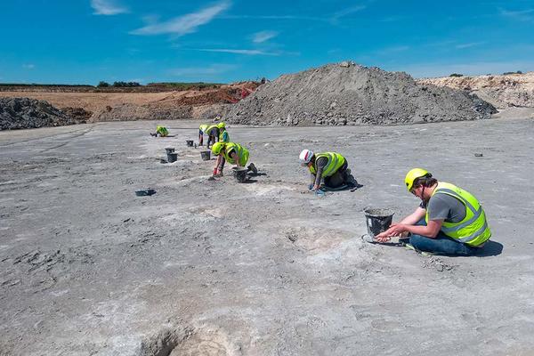 Seven people in hi-viz jackets excavating dinosaur footprints in a quarry